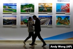 Trecători pe lângă un panou care prezintă proiectele de construcție ale Chinei la centrul media al Inițiativei Belt and Road din Beijing.